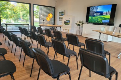 Chambre lumineuse avec lit double, bureau, coin salon, kitchenette et vue sur un jardin à travers une baie vitrée.