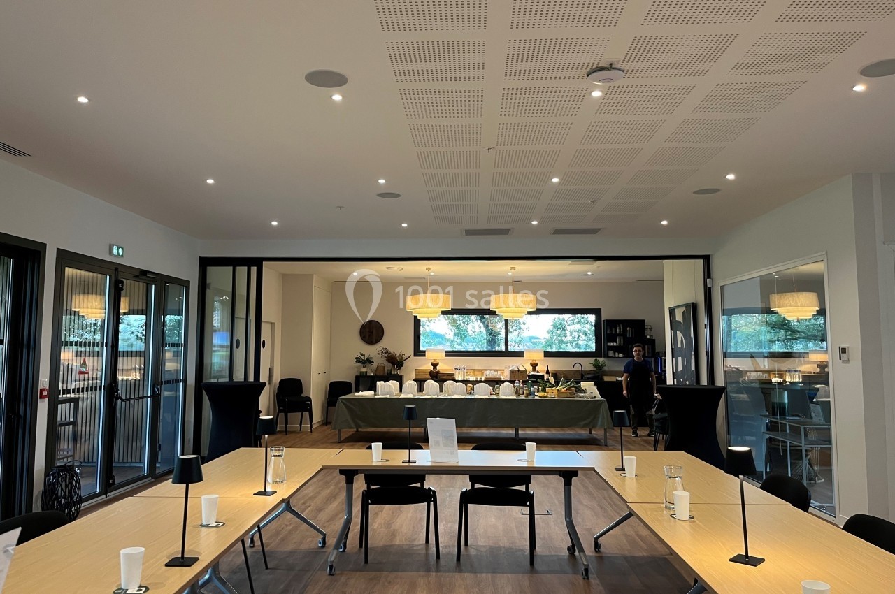 Salle de réunion lumineuse avec tables en U, bougies décoratives et buffet dressé en arrière-plan.