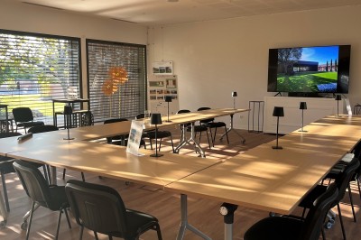 Chambre lumineuse avec lit double, bureau, coin salon, kitchenette et vue sur un jardin à travers une baie vitrée.