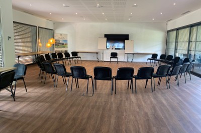 Chambre lumineuse avec lit double, bureau, coin salon, kitchenette et vue sur un jardin à travers une baie vitrée.