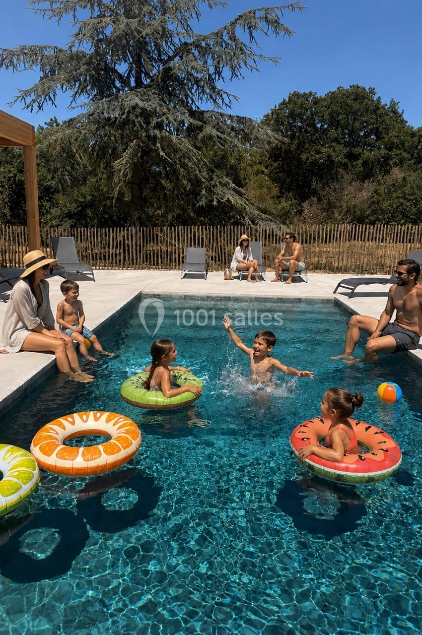 Des enfants jouent avec des bouées dans une piscine, entourés d'adultes assis sur les bords par une journée ensoleillée.