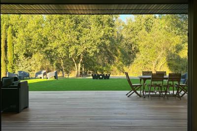 Terrasse moderne avec mobilier en plastique et bois, entourée de verdure et partiellement ombragée par un arbre.