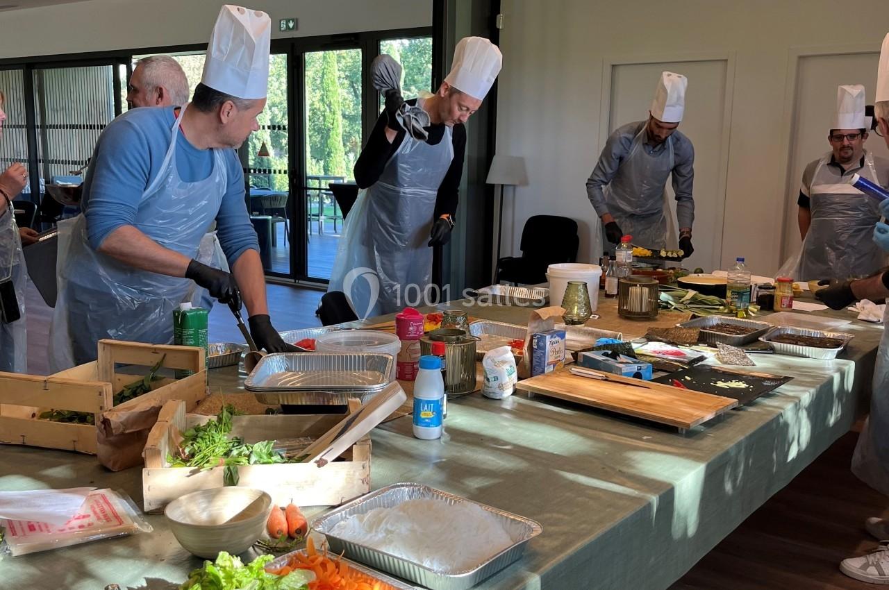 Des personnes en tabliers et toques cuisinent ensemble autour d'une grande table garnie d'ingrédients et d'ustensiles.