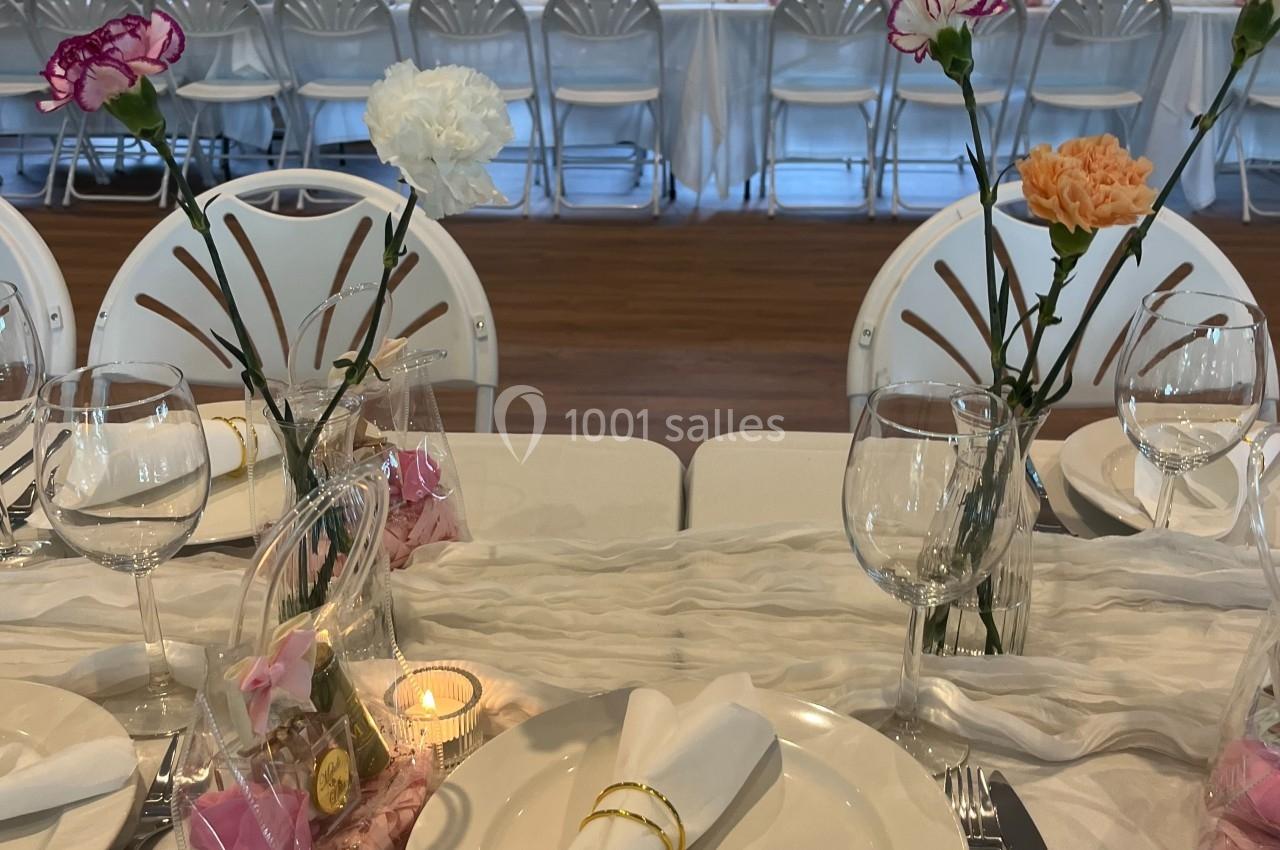 Table dressée pour un événement, avec assiettes, serviettes pliées, verres, fleurs en vase et invités en arrière-plan.