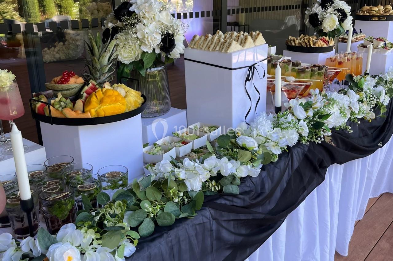 Table de buffet décorée avec des fleurs blanches, nappes élégantes et une variété de plats et boissons.