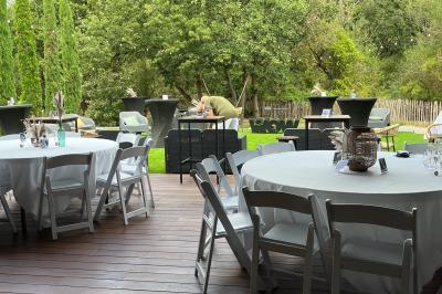 Terrasse moderne avec mobilier en plastique et bois, entourée de verdure et partiellement ombragée par un arbre.