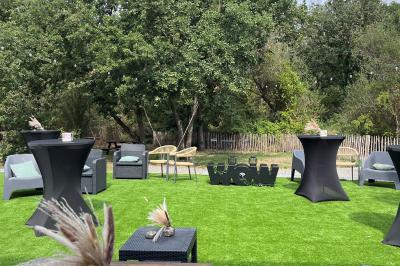 Terrasse moderne avec mobilier en plastique et bois, entourée de verdure et partiellement ombragée par un arbre.