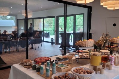 Terrasse moderne avec mobilier en plastique et bois, entourée de verdure et partiellement ombragée par un arbre.