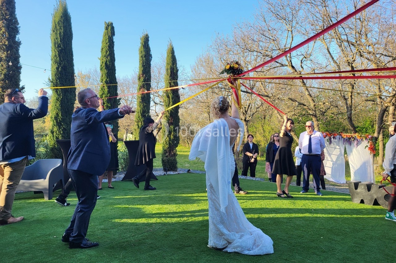 Des invités entourent une mariée tenant des rubans colorés lors d'une animation en plein air sur une pelouse.