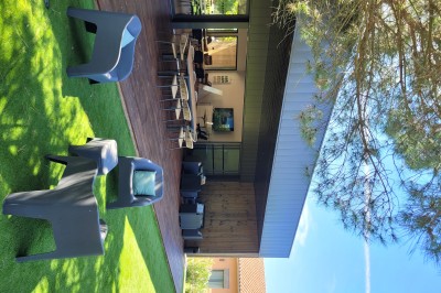 Terrasse moderne avec mobilier en plastique et bois, entourée de verdure et partiellement ombragée par un arbre.
