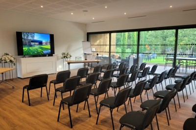 Chambre lumineuse avec lit double, bureau, coin salon, kitchenette et vue sur un jardin à travers une baie vitrée.