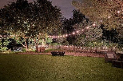 Chambre lumineuse avec lit double, bureau, coin salon, kitchenette et vue sur un jardin à travers une baie vitrée.