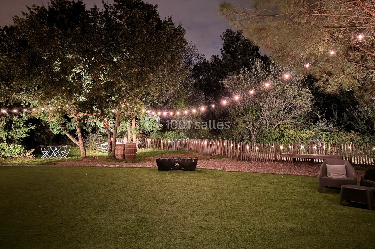 Guirlandes lumineuses suspendues au-dessus d'un jardin avec pelouse, arbres, clôture en bois et mobilier extérieur.