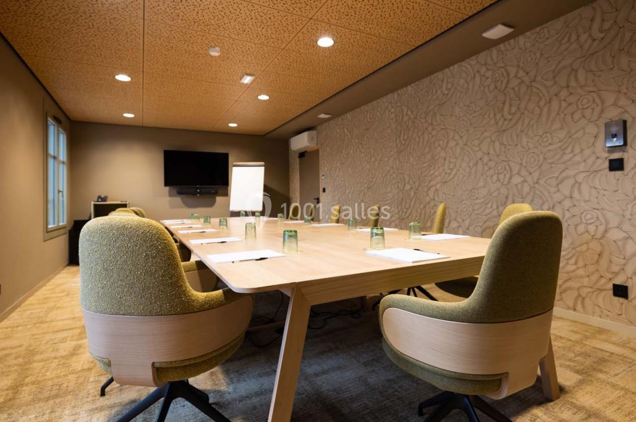 Salle de réunion moderne avec table en bois, chaises vertes, écran mural, paperboard et lumière naturelle.