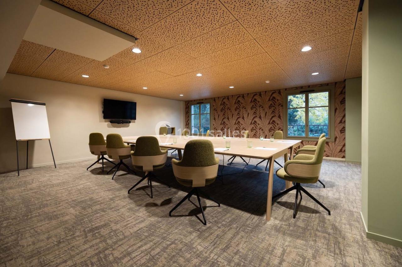 Salle de réunion moderne avec table rectangulaire, chaises vertes, écran mural, tableau blanc et fenêtres donnant sur un…