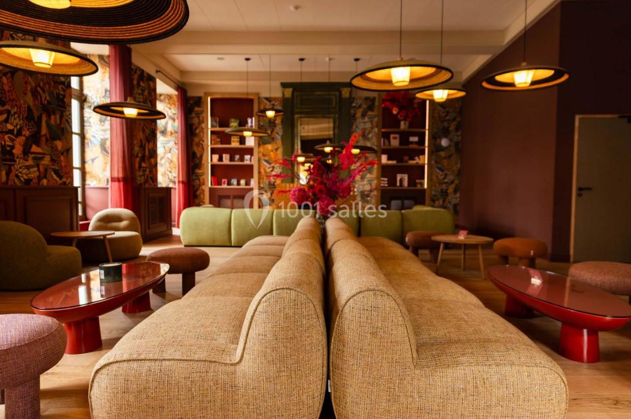 Salon chaleureux avec canapés beiges, tables basses rouges, luminaires suspendus et décorations florales vives.