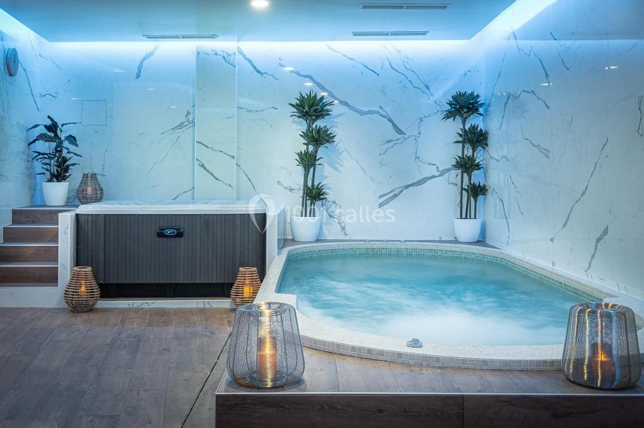 Jacuzzi et spa intérieur entourés de plantes et de murs en marbre, éclairage tamisé et ambiance relaxante.