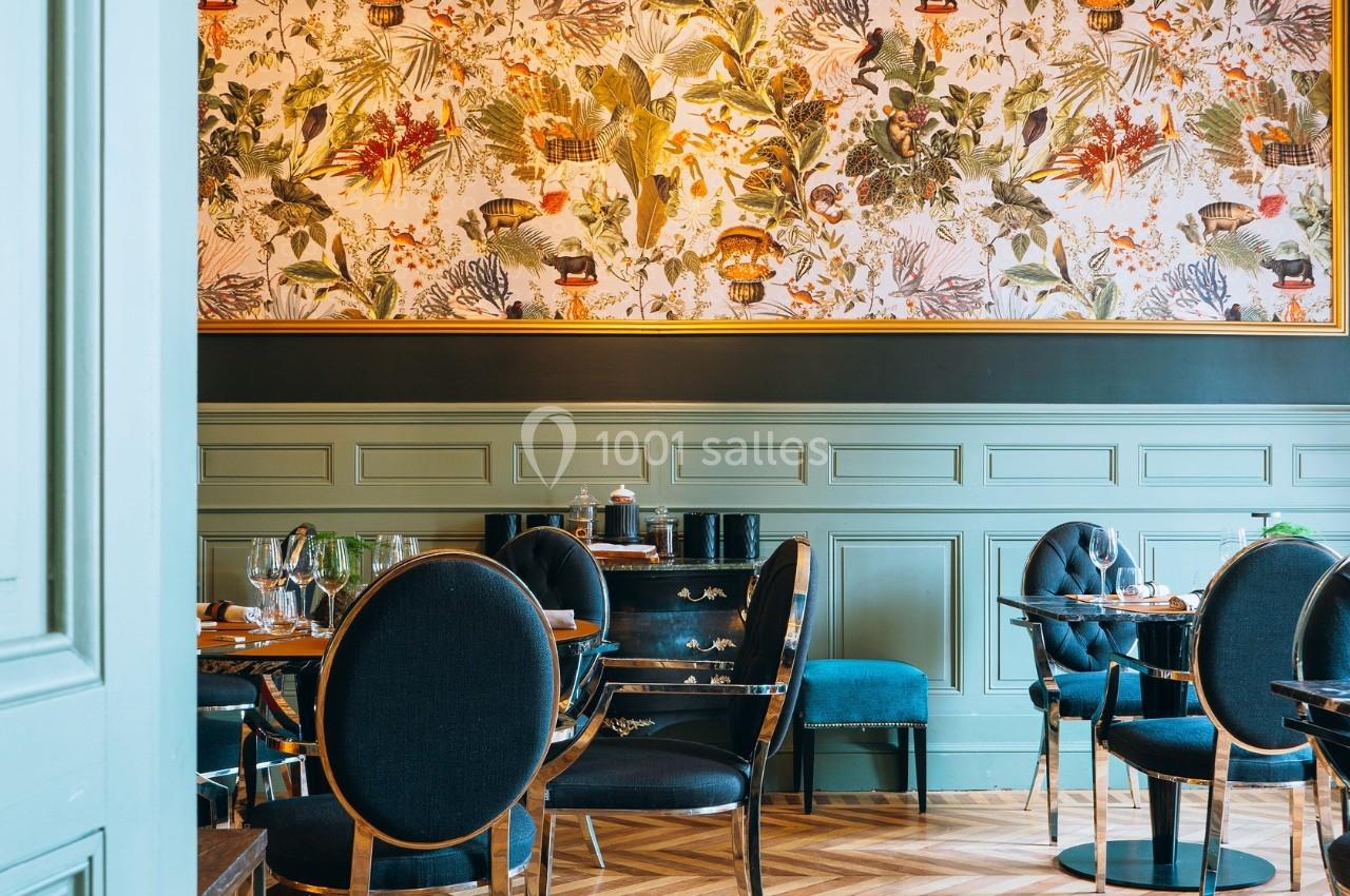 Salle de restaurant élégante avec murs ornés de boiseries vertes et papier peint à motifs végétaux colorés.