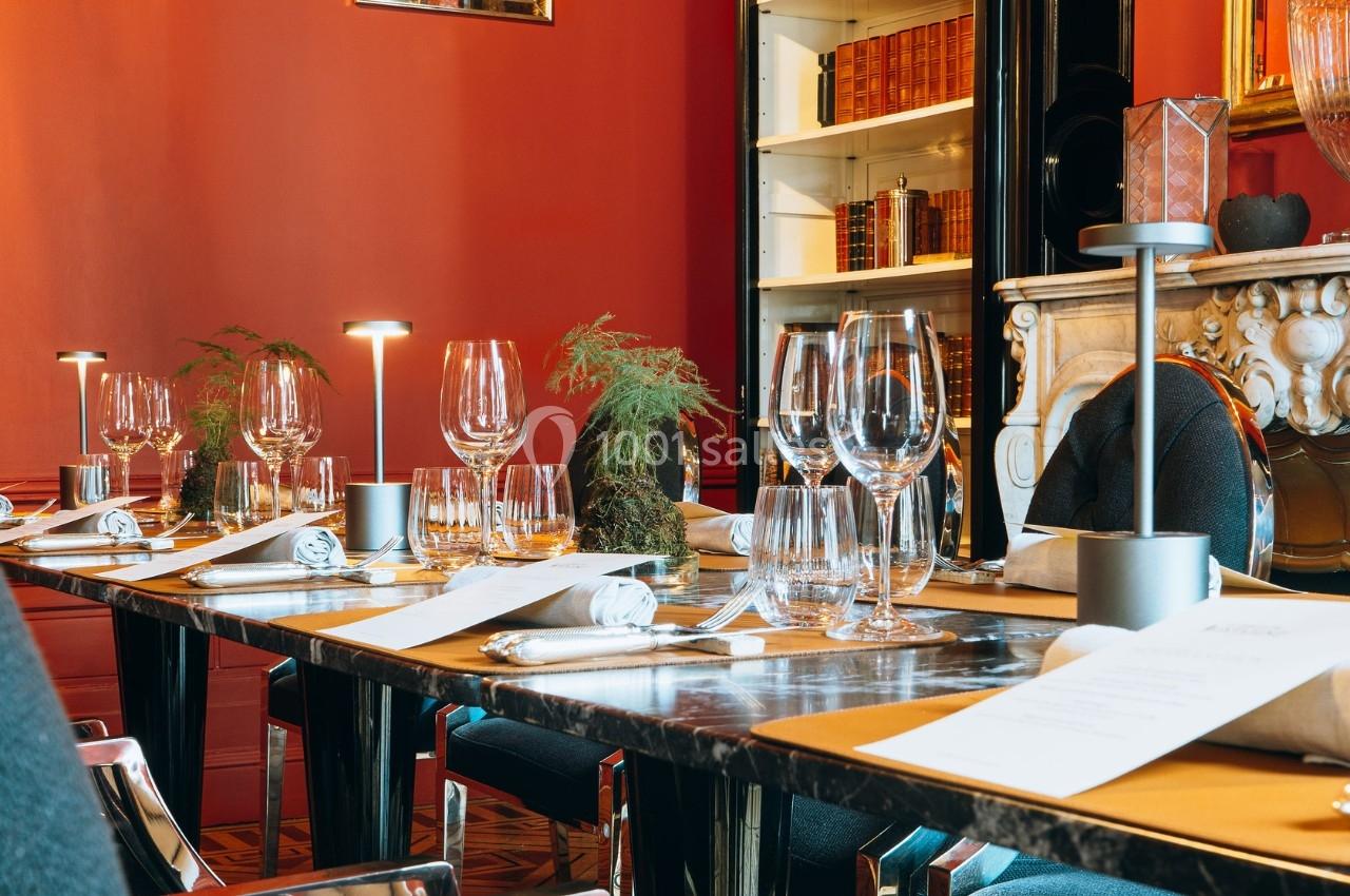 Table élégamment dressée dans un restaurant avec murs rouges, livres en arrière-plan et éclairage tamisé.