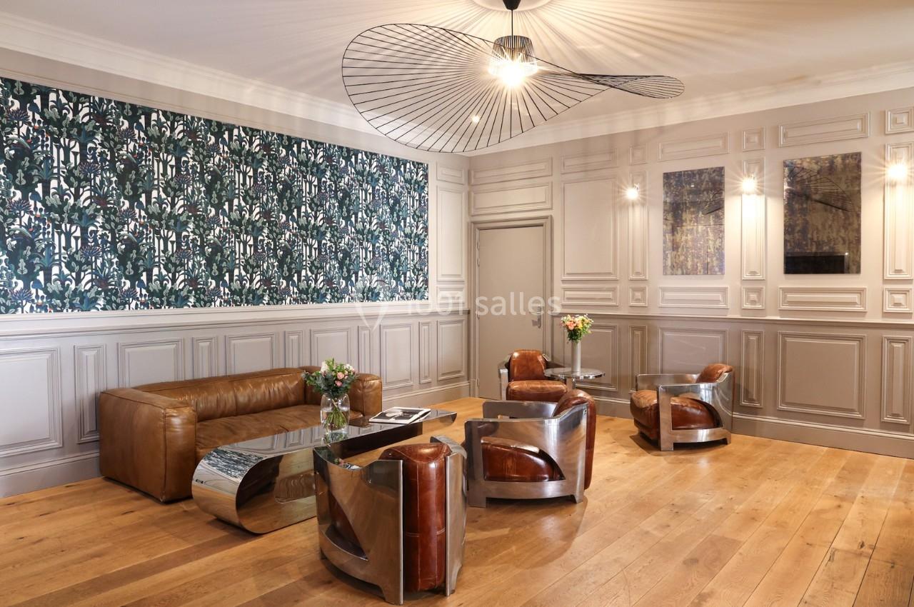 Salon élégant avec fauteuils en cuir, tables basses métalliques, parquet en bois clair et mur décoré de papier peint floral.