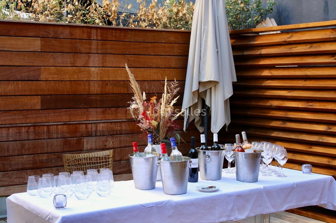 Table dressée en extérieur avec bouteilles de vin, seaux à glace, verres et décoration florale sur fond de bois.