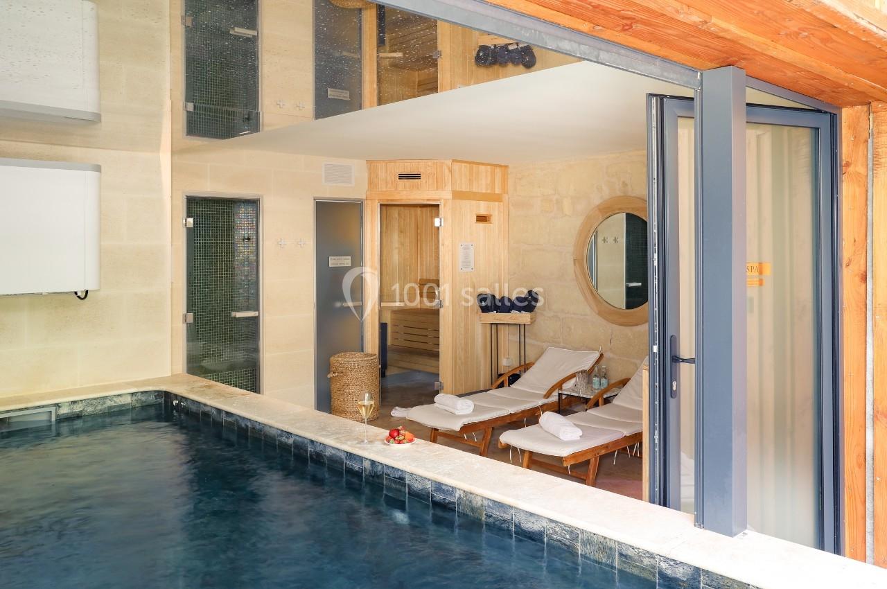 Espace spa avec piscine intérieure, chaises longues, serviettes blanches et murs en pierre beige.