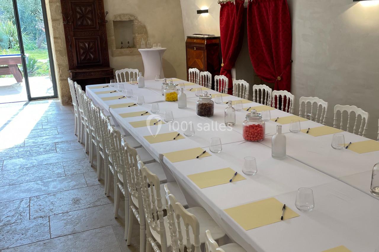 Salle voûtée aménagée pour une réunion, avec une longue table dressée de blocs-notes, verres et chaises blanches.