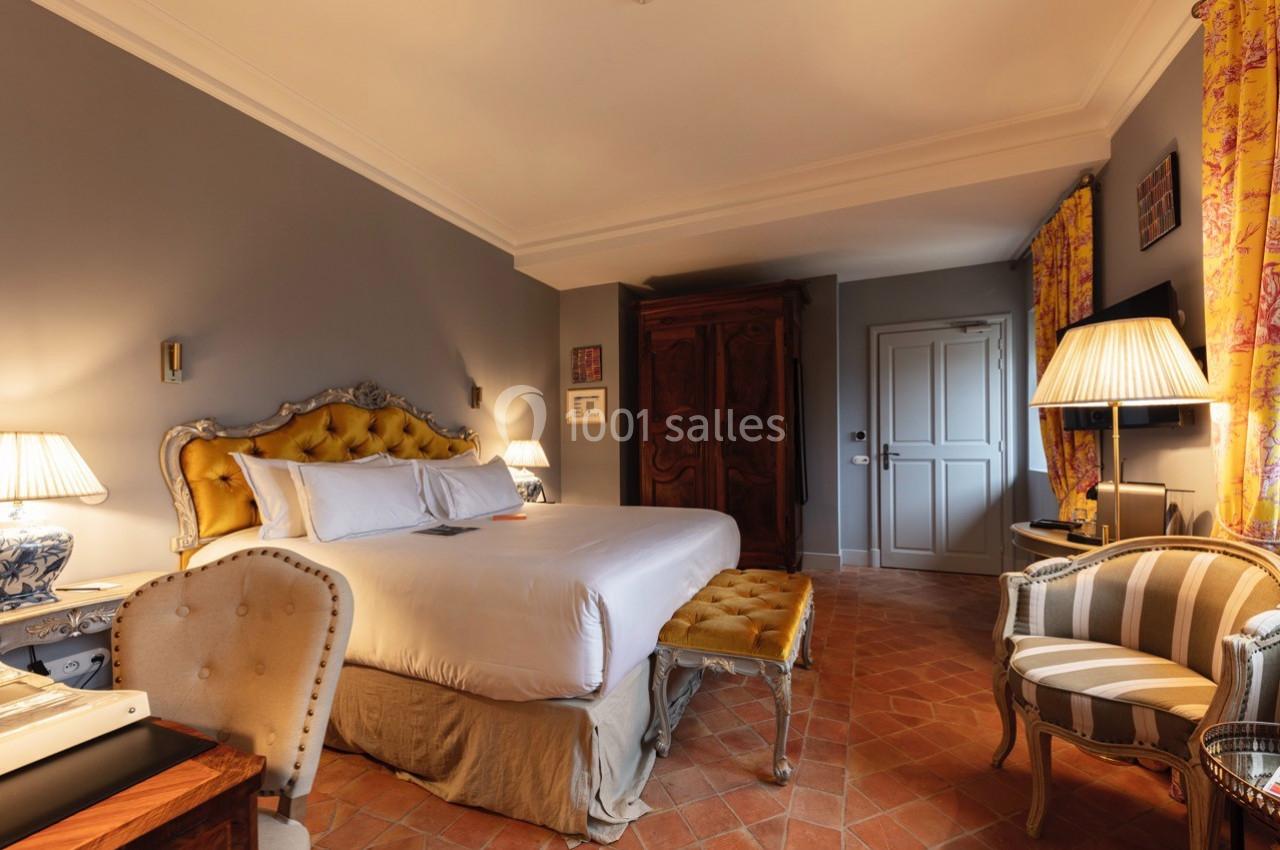 Chambre élégante avec lit double, mobilier classique, murs gris, sol en terre cuite et lumière tamisée.