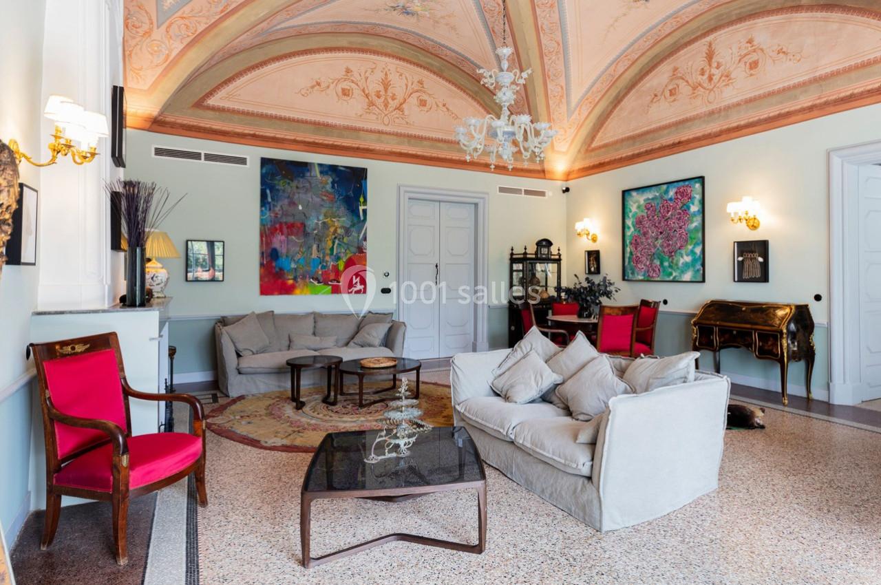 Salon élégant avec plafond voûté peint, mobilier classique, œuvres d'art colorées et lumière naturelle abondante.