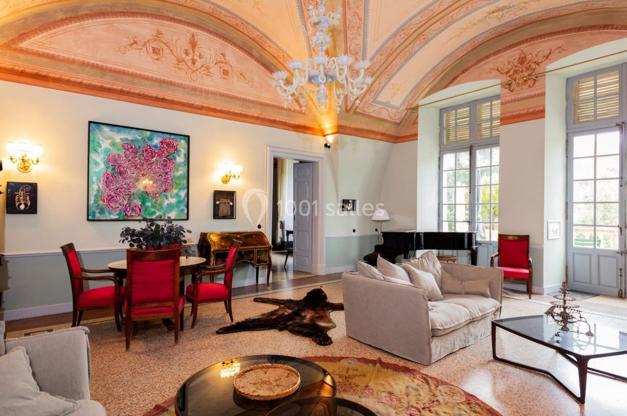 Salon élégant avec fresques au plafond, mobilier classique, piano à queue et grandes fenêtres laissant entrer la lumière.