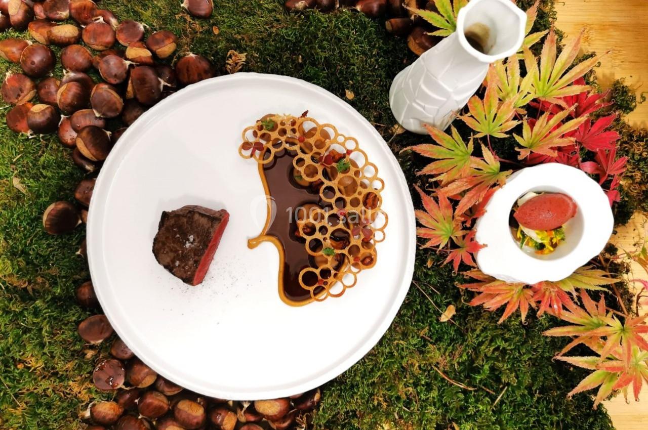 Assiette gastronomique avec viande, sauce, décorations croustillantes, présentée sur mousse, châtaignes et feuilles d…