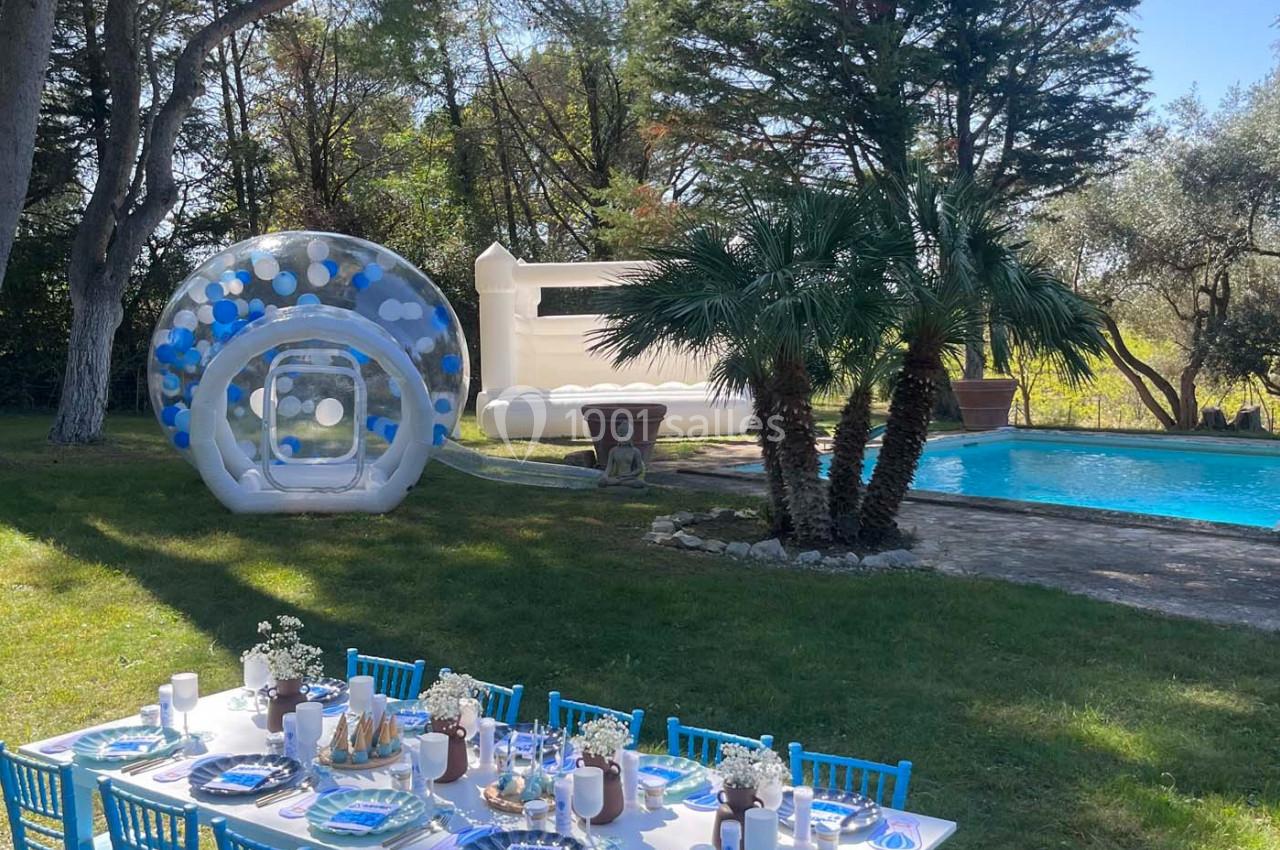 Table dressée avec des chaises bleues dans un jardin près d'une piscine, décorée pour une fête avec des ballons et un…