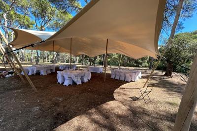 Grand chapiteau beige éclairé par des guirlandes lumineuses, abritant des tables rondes dressées pour un événement en plein…