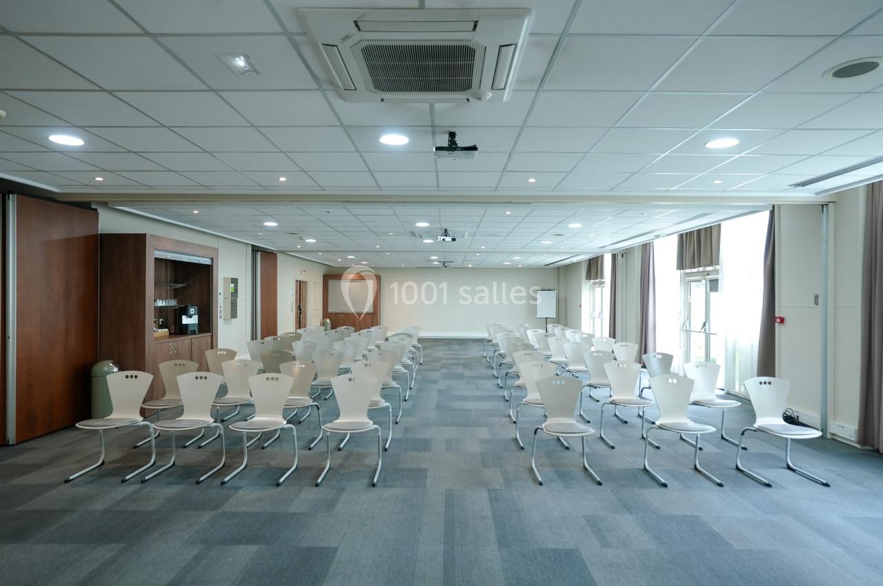 Salle de conférence lumineuse avec des rangées de chaises blanches alignées, prête pour une présentation ou un événement.