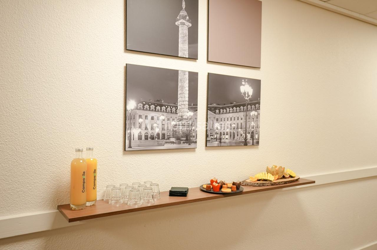 Plateau avec jus d'orange, verres, morceaux de fruits et viennoiseries sur une étagère, devant des photos murales.