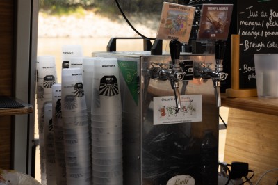 Fontaine à bière avec gobelets réutilisables empilés, posée sur un comptoir en bois près d'un tableau de menu.