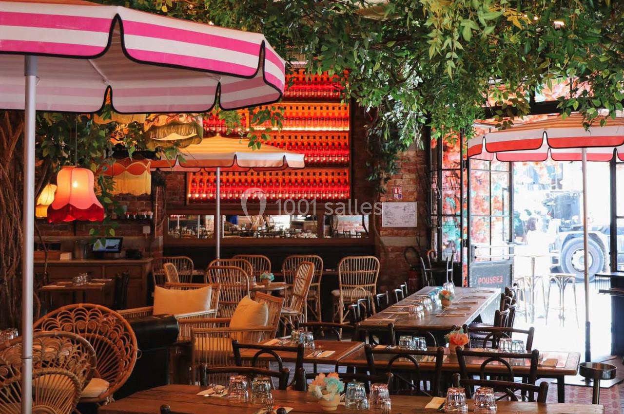Salle de restaurant décorée avec des parasols colorés, des plantes suspendues et des tables en bois dressées.