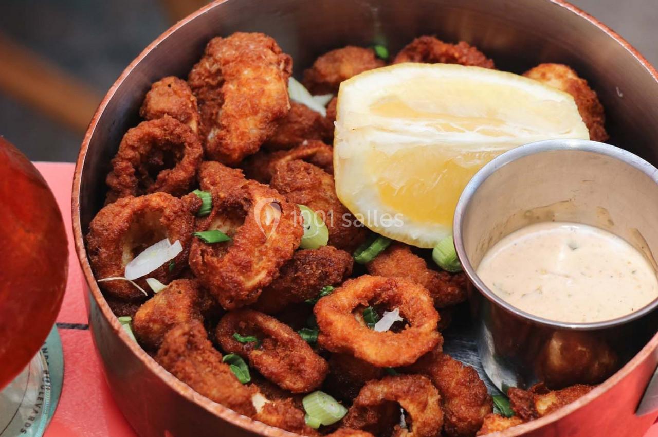 Calamars frits servis avec une tranche de citron et une sauce crémeuse dans un bol en métal.