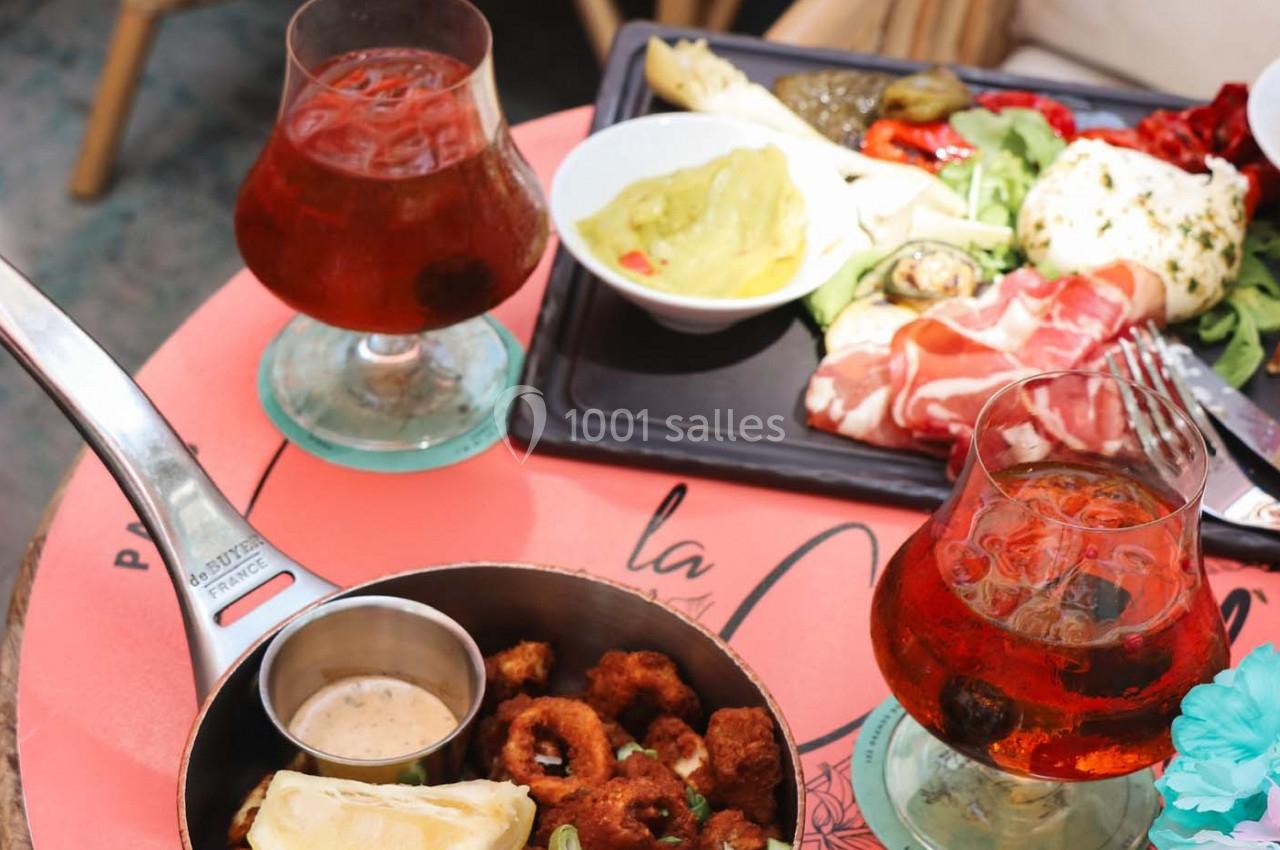 Assiette de charcuterie et burrata, calamar frit avec sauce, et deux verres de boisson ambrée sur une table rose.