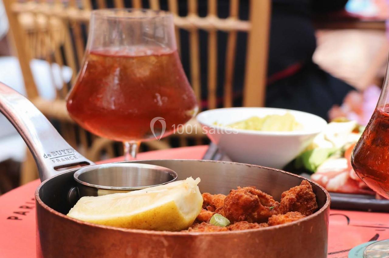 Plat de beignets servis dans une casserole en cuivre avec un quartier de citron, accompagné de boissons et d'accompagnements.