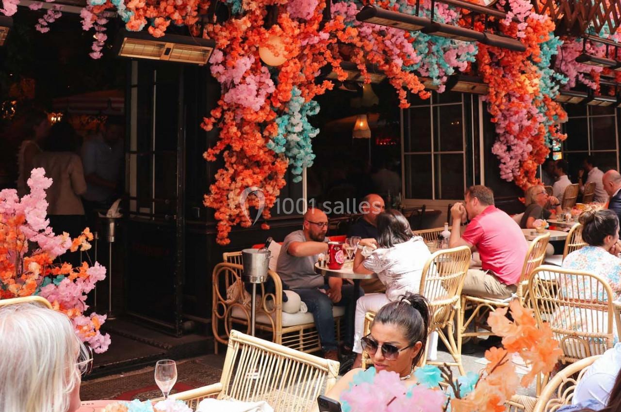 Terrasse d'un café décorée de fleurs colorées, avec des clients assis à des tables en plein air.