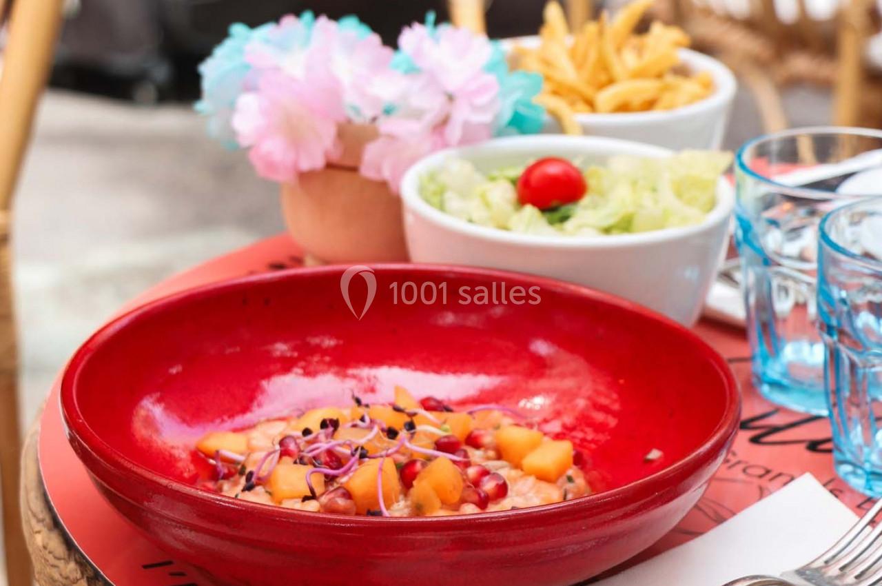 Assiette de salade colorée avec fruits et graines, accompagnée de frites et d'une salade verte sur une table en terrasse.