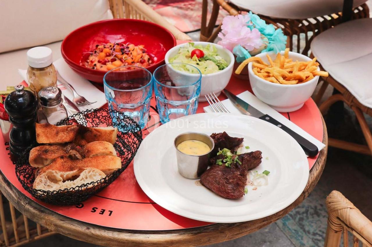 Assiette de viande avec sauce, pain, salade, frites et accompagnements sur une table en terrasse.