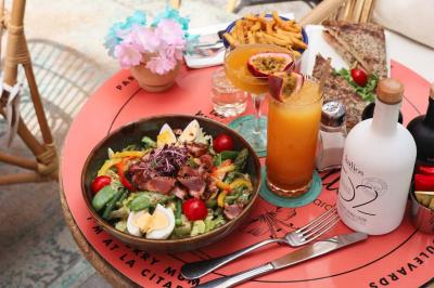 Plateau avec un café, un cannelé, une tartelette, une brioche, de la crème et des verres sur une table rouge.