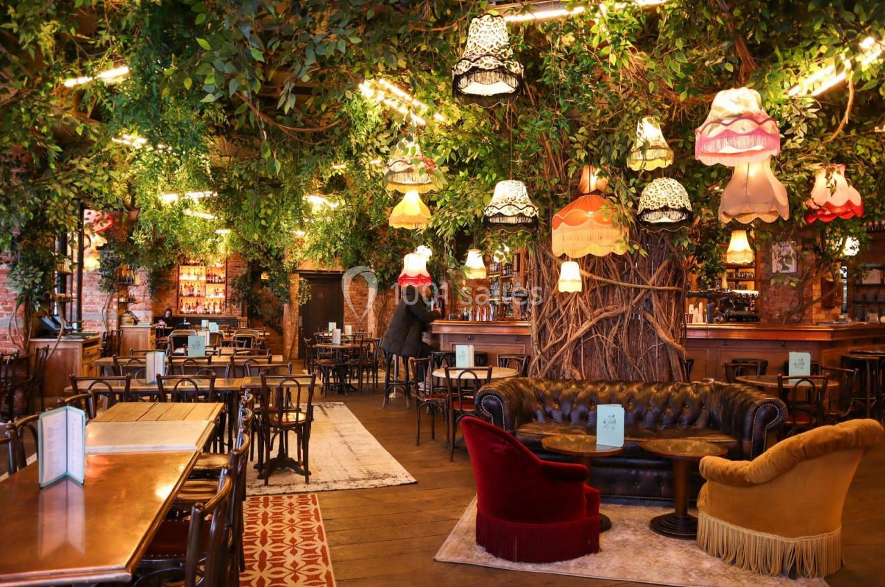 Salle de restaurant décorée avec des plantes suspendues, des luminaires vintage et un mobilier éclectique.