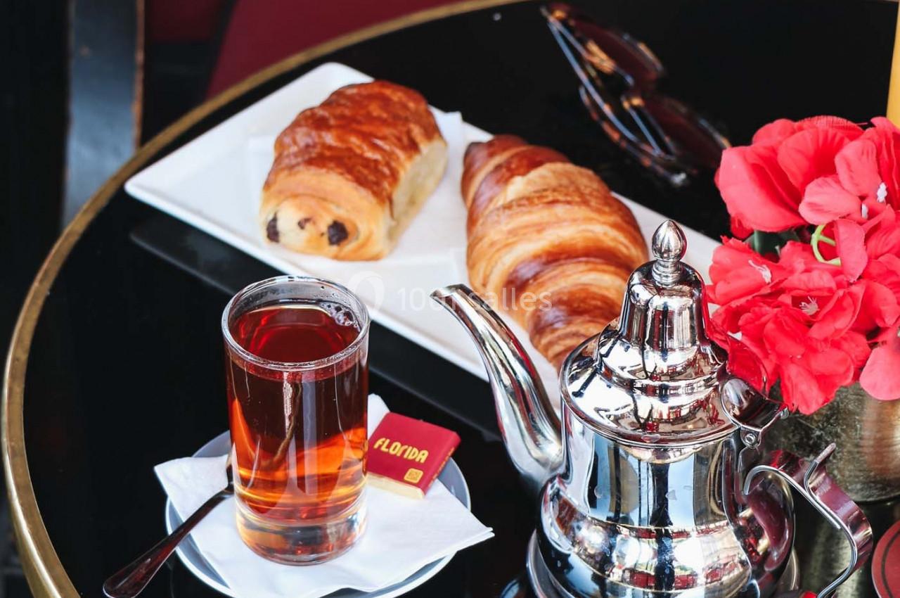 Petit-déjeuner avec thé, croissant, pain au chocolat et fleurs rouges sur une table noire dans un café.