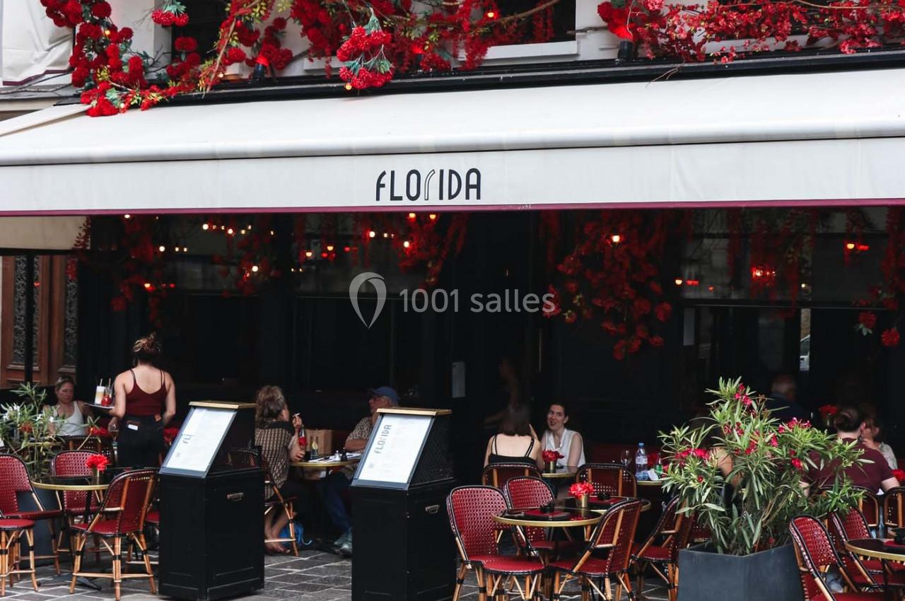 Terrasse d’un café-restaurant avec des tables occupées, façade ornée de fleurs rouges et enseigne ’Florida’.