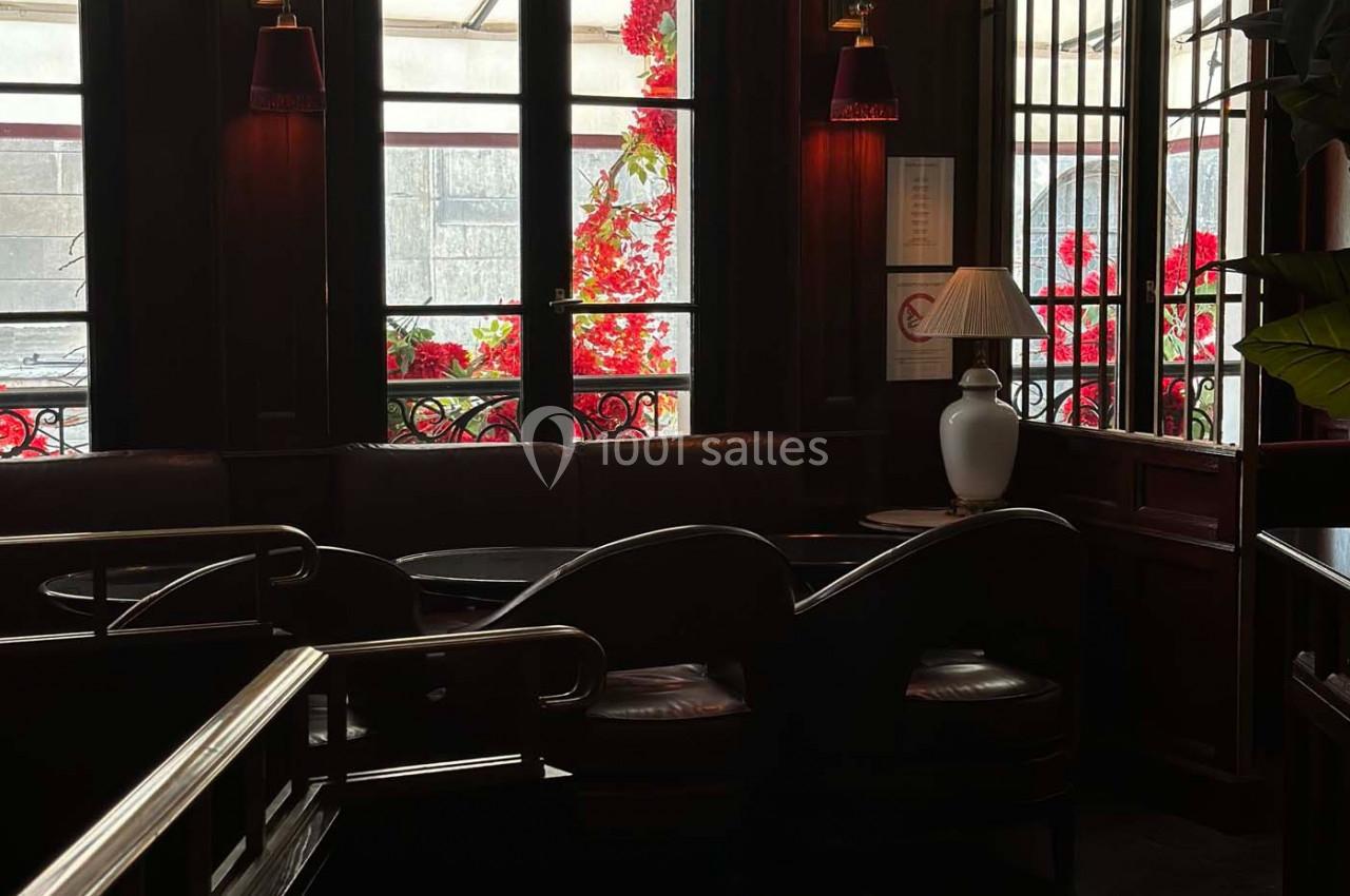 Intérieur sombre d'un café avec des banquettes, des fenêtres donnant sur des fleurs rouges et une lampe allumée.