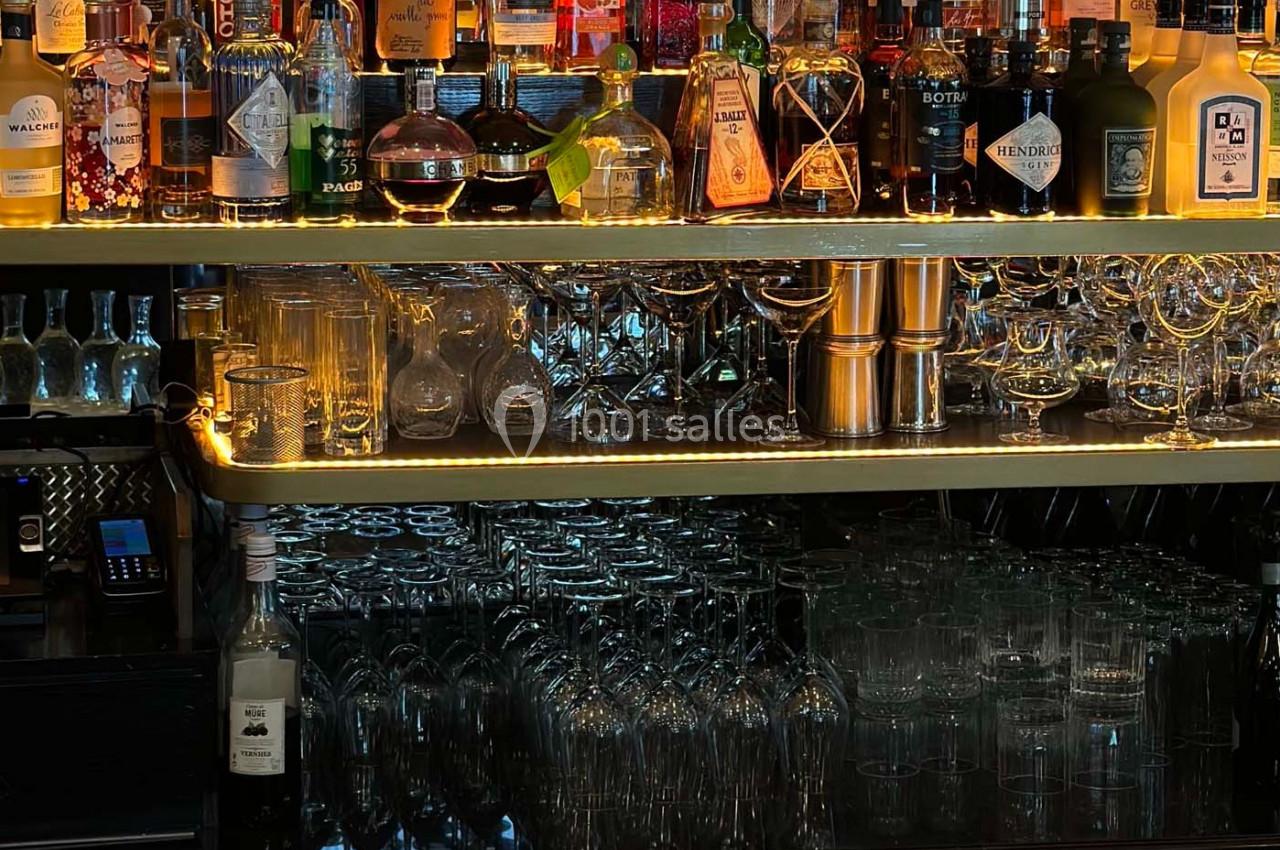 Étagères de bar avec une variété de bouteilles d'alcool, verres suspendus et éclairage tamisé.