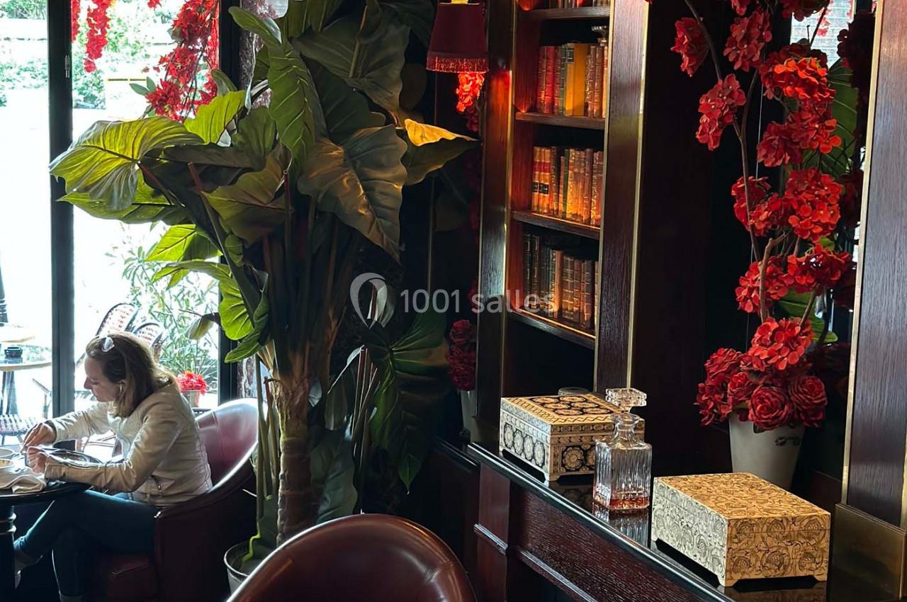 Intérieur d'un café élégant avec fauteuils en cuir, plantes, étagères décorées et lumière tamisée.